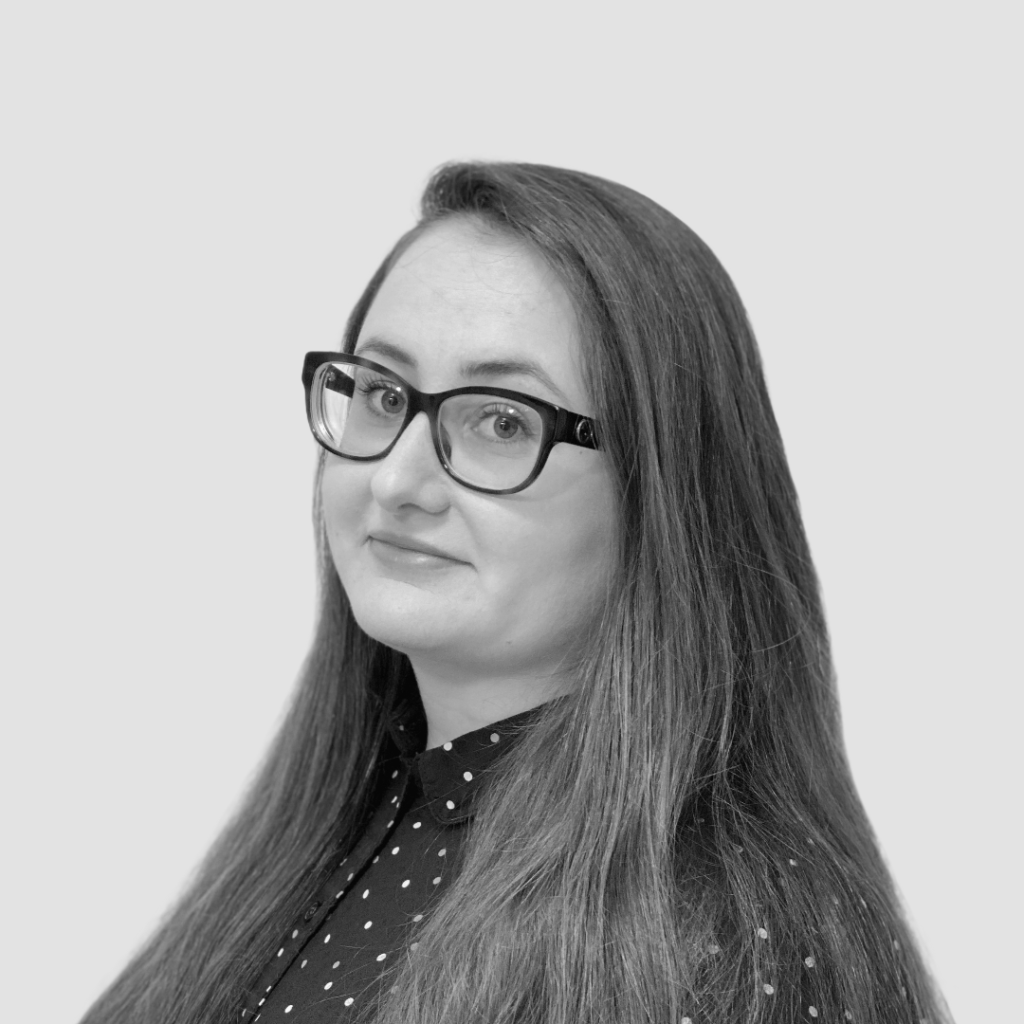 Black and white headshot of Danielle Gleicher-Bates, a smiling white woman with long hair and glasses.
