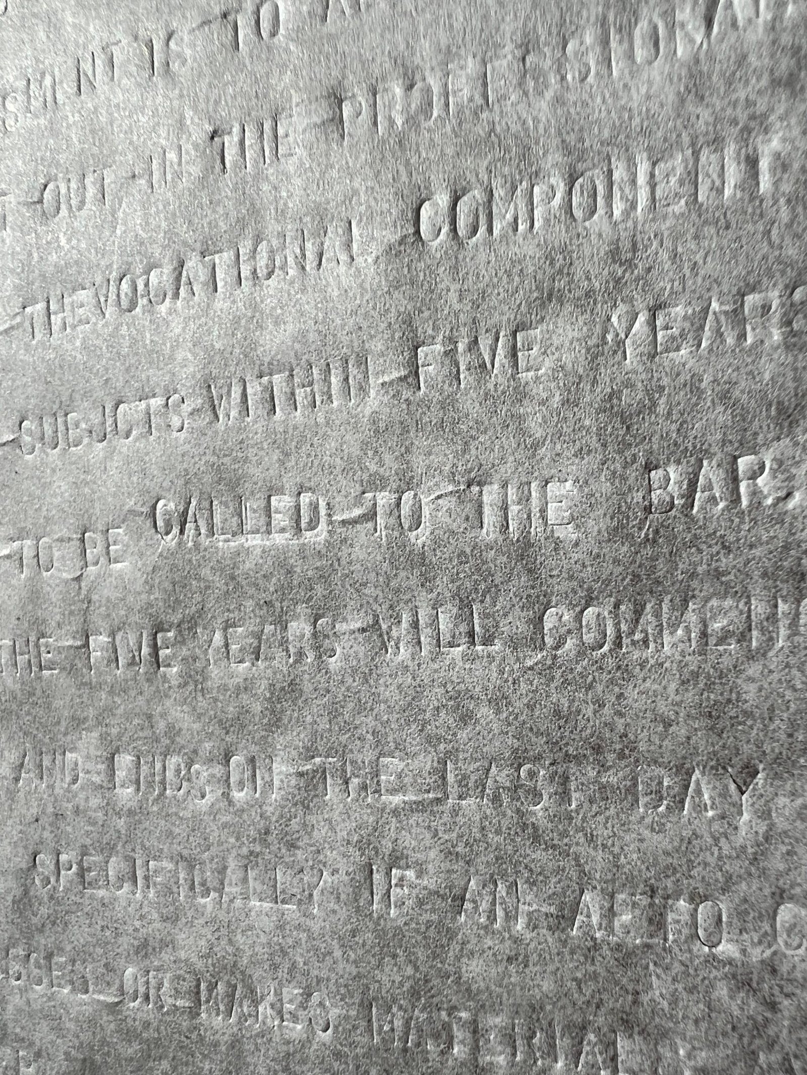 A close-up photograph of a large sheet of parchment paper which has been blind debossed with uppercase text in a font similar used by typewriters. The translucency and lack of ink make the debossed text visible but illegible except at specific angles, under certain light, and on close inspection. The photograph and lighting are angled enabling the words to be deciphered. The physical process of hand-debossing the fragile paper has created light crumpling and depressed areas, in addition to the texture created by each individual character.